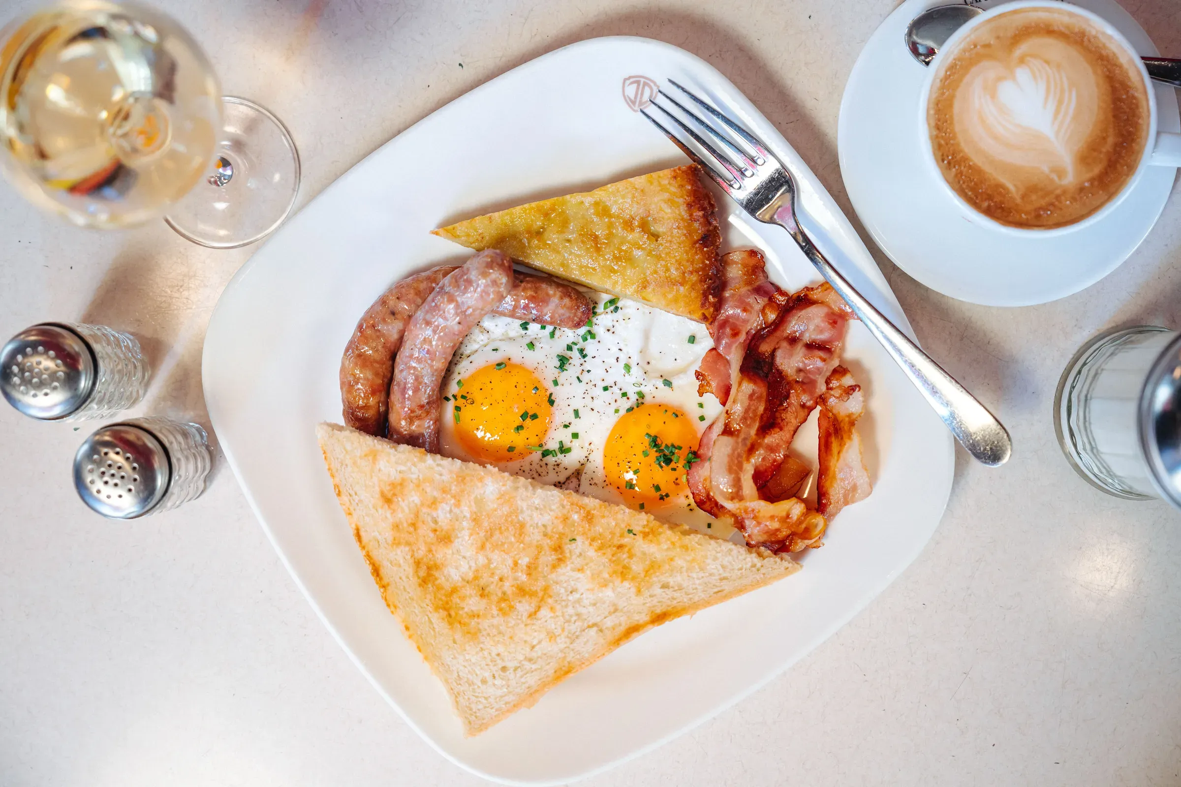Americká snídaně shora: sázená vejce, slanina, klobásky, toast a cappuccino