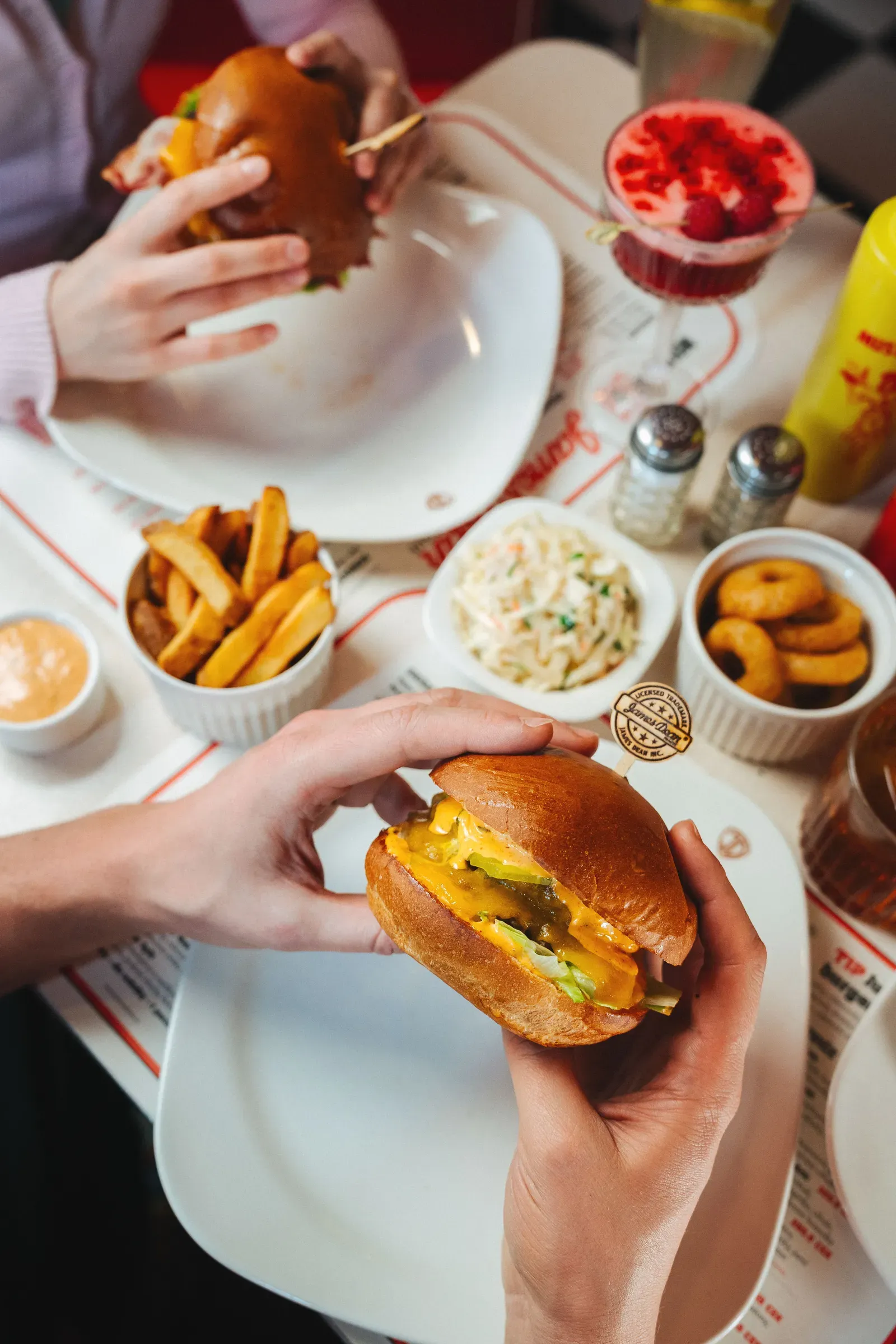 Burger v ruce, k tomu hranolky, coleslaw a cibulové kroužky