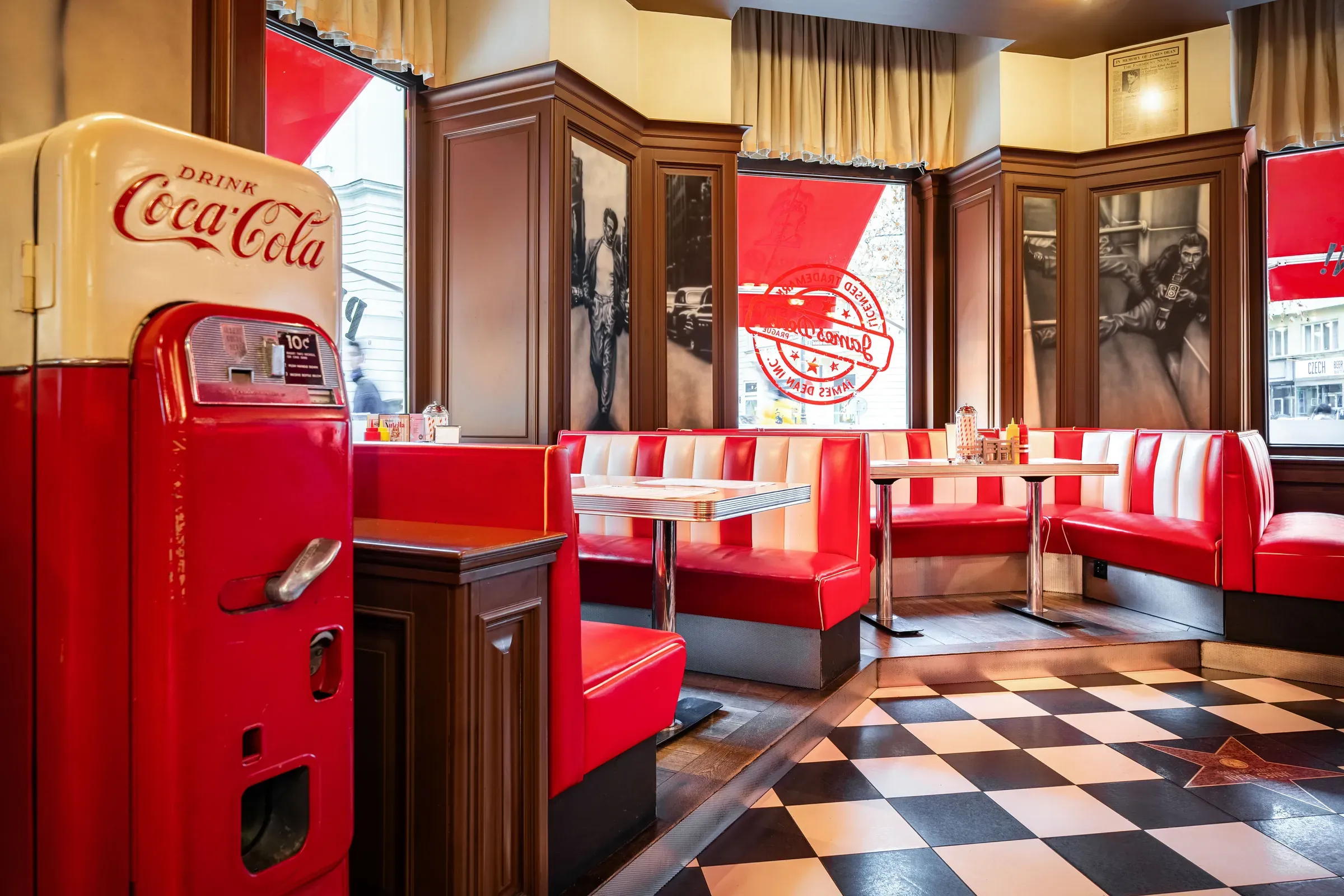 Červené boxy u oken a retro automat Coca-Cola na šachovnicové podlaze