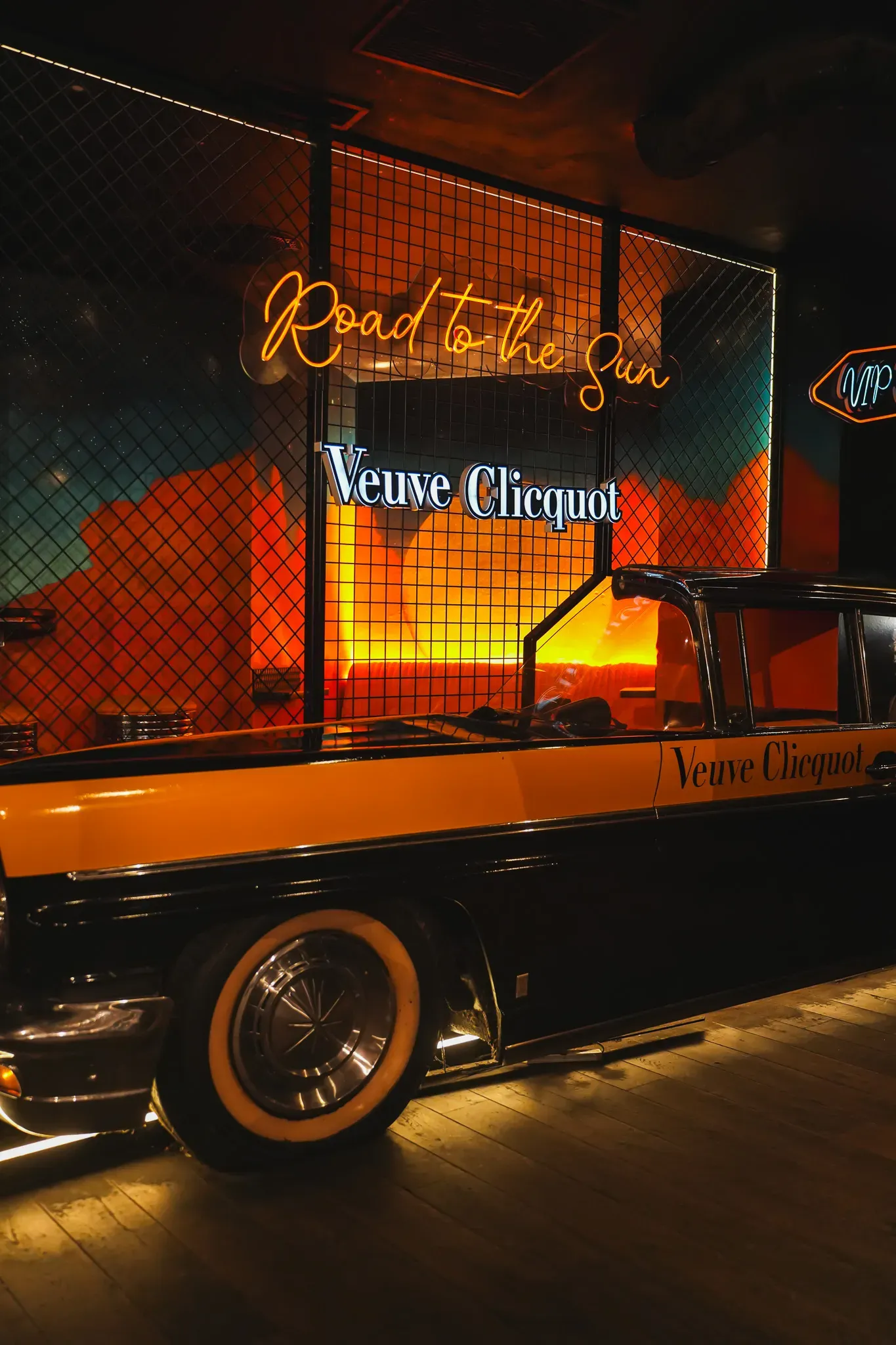 Černožluté americké auto pod neonem Road to the Sun ve VIP zóně Music Clubu