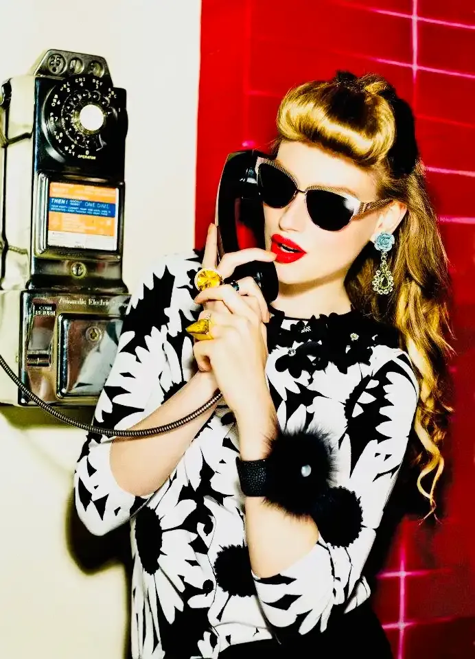Modelka ve slunečních brýlích telefonuje z nástěnného retro telefonu