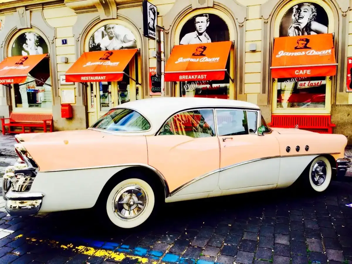 Průčelí James Dean Prague s oranžovými markýzami a růžovobílý americký veterán před vchodem